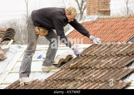 Un costruttore di montaggio di piastrelle su un tetto di una casa in estensione Foto Stock
