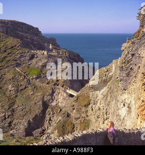 Giovane donna ammirando scogliere soleggiato vista serale con passerella e sentieri scoscesi a Tintagel Castle Cornwall Inghilterra Foto Stock