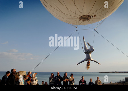 Un gigante palloncino elio con un' antenna trapezista sospeso sotto deviati al di sopra di spettatori in Dorset s Jurassic Coast Arts Foto Stock