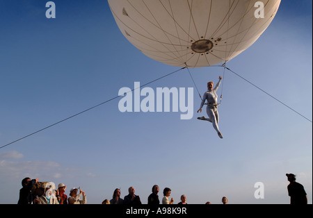 Un gigante palloncino elio con un' antenna trapezista sospeso sotto deviati al di sopra di spettatori in Dorset s Jurassic Coast Arts Foto Stock