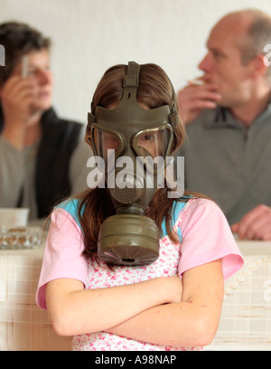 Una giovane ragazza è indossare una maschera a gas demonstratively perché i suoi genitori sono fumatori nella stessa camera Foto Stock