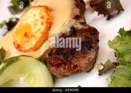 Bistecca alla griglia con formaggio fuso e uova fritte, guarnita con verdure miste, fette di cetriolo e peperone su un piatto bianco. Foto Stock