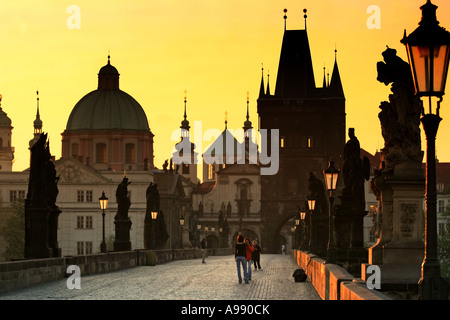 L'ora d'oro bagna l'iconico Ponte Carlo di Praga con un caldo bagliore, mentre le statue sagomate sono di guardia sulla tranquilla scena mattutina Foto Stock