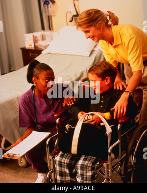African American nurse parlando con il ragazzo giovane paziente in sedia a rotelle e sua madre Foto Stock