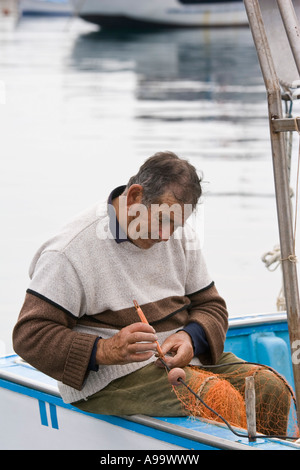 Pescatore siciliano seduti in barca rammendo reti da pesca al Marina sul Mar Tirreno Cefalù Sicilia Italia Foto Stock