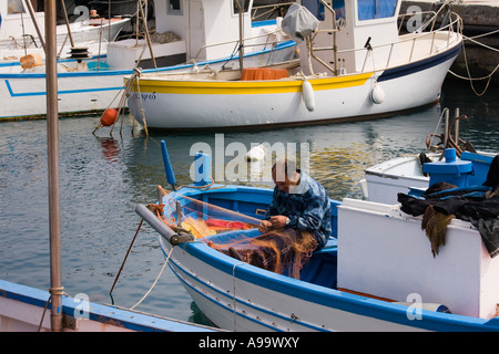 Pescatore siciliano si siede in barca rammendo reti da pesca al Marina sul Mar Tirreno Cefalù Sicilia Italia Foto Stock