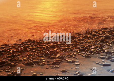 La luce del tramonto che colpisce acqua e ciottoli lungo la Pacific Ocean Shore Foto Stock