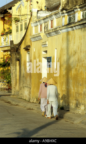 Due signore in conica cappelli non camminando lungo Bach Dang St, nelle prime ore del mattino, Hoi An, Viet Nam Foto Stock