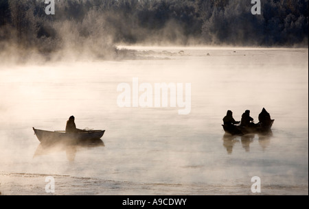 I pescatori che scorgono il bianco dalle barche a remi / sciatori / gommoni a freddo giorno d'inverno al fiume Oulujoki Oulu , Finlandia Foto Stock