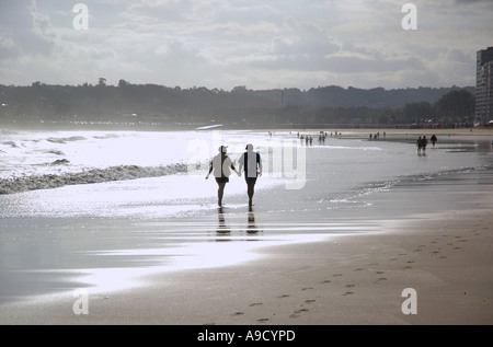 Un giovane camminando mano nella mano lungo il lungomare e la spiaggia di Gijon Xixon Asturias Golfo di Biscaglia Spagna España Europa Foto Stock