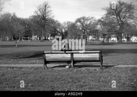 Vista di Hendon Park con la giovane donna seduta su un banco di lavoro nel nord di Londra England Regno Unito Europa Foto Stock