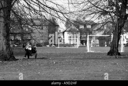 Vista di Hendon Park con anziani donna seduta su un banco di lavoro quotidiano di lettura nel nord di Londra England Regno Unito Europa Foto Stock