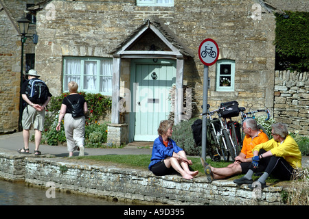 Cylists sulla banca degli occhi in Lower Slaughter Gloucestershire Cotswold area England Regno Unito Regno Unito Foto Stock