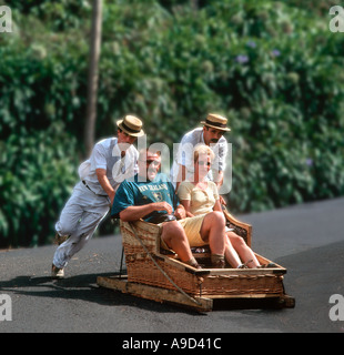 Coppia di mezza età che viene spinto in una pista da slittino tradizionale tra monte e Funchal, Madeira, Portogallo Foto Stock