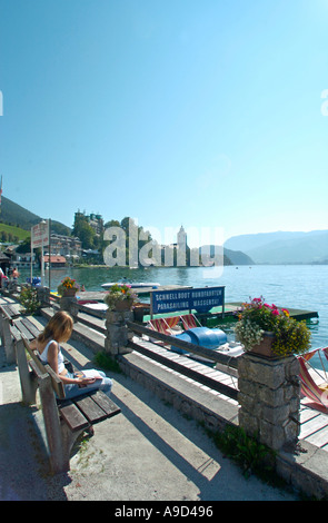 Giovane donna seduta su una panchina sul lungolago in St Wolfgang, lago di Wolfgang, Salzkammergut, Austria Foto Stock