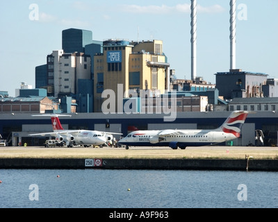 London City Airport British Airways aeromobile la tassazione sulla pista con Tate and Lyle Silvertown raffineria di zucchero al di là nei Docklands di Londra Inghilterra REGNO UNITO Foto Stock