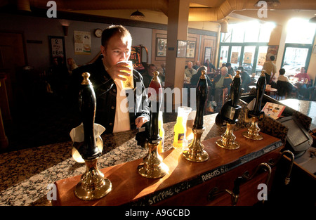 Un uomo che affonda una tranquilla pinta in un tradizionale pub inglese in un pomeriggio soleggiato Foto Stock