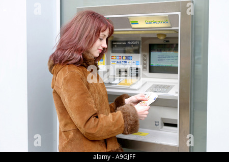 I capelli rossi donna su automatic teller machine, tenendo le banconote in una mano. Foto Stock