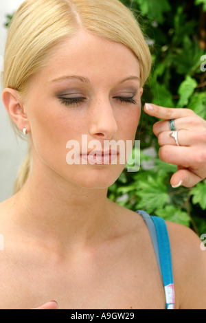 Donna bionda con gli occhi chiusi, mano di altra donna toccando le ciglia. Foto Stock