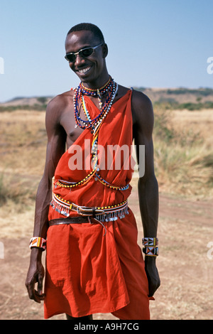 Un uomo Masai in abito tradizionale pone indossando occhiali da sole nel Masai Mara in Kenya. Foto Stock