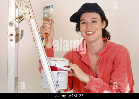 Giovane donna tenendo un pennello in piedi accanto alla scaletta Foto Stock