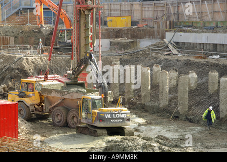 Sito in costruzione escavatore meccanico lavorando al fianco di pila alesatrice il caricamento di massa di impasto dalla coclea al dumper Foto Stock