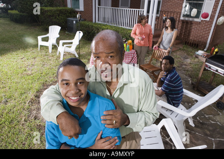 Padre e figlio godendo il barbecue nel cortile con la famiglia in background Foto Stock