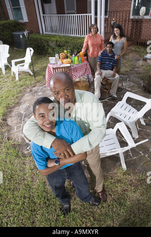 Padre e figlio godendo il barbecue nel cortile con la famiglia in background Foto Stock