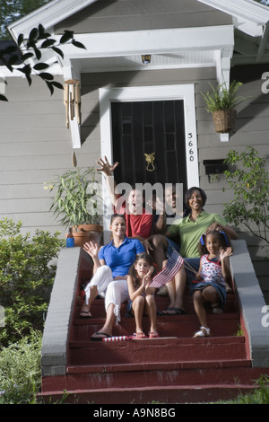Ritratto di due famiglie seduti sui gradini di fronte a una casa sventolando bandiere statunitensi Foto Stock