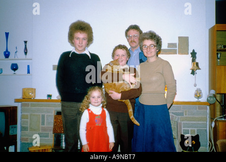 ritratto di famiglia degli anni '1970 nel soggiorno di una casa domestica: genitori, due ragazzi di 13 e 11 anni, una bambina di 4 anni e il loro gatto zenzero Foto Stock