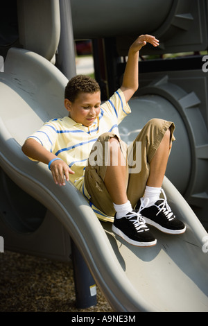 Ragazzo in un parco giochi lo scorrimento verso il basso una diapositiva Foto Stock