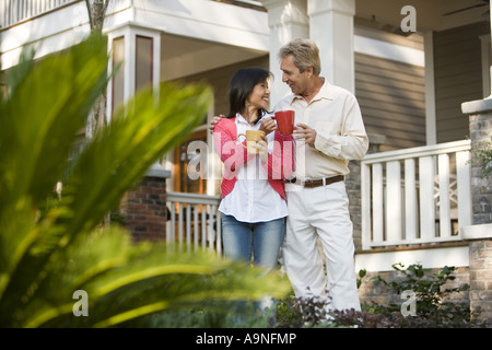 Affettuosa coppia inter-razziale giovane azienda tazze da caffè davanti alla loro casa Foto Stock