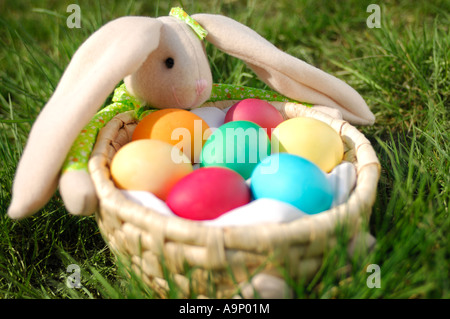 Coniglietto di pasqua in erba con un cesto pieno di uova colorate Foto Stock