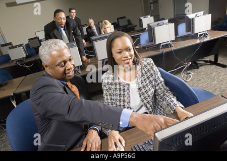 Uomo anziano aiutando più giovane collega di lavoro in laboratorio informatico Foto Stock