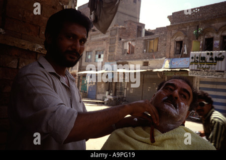 Un barbiere pakistano la rasatura a un cliente per le strade di Rawalpindi Foto Stock