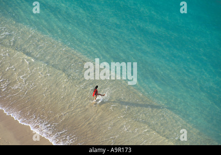 Donna che cammina in chiare acque costiera lungo la spiaggia di Waikiki di Oahu Island in Hawaii presso sunrise Foto Stock