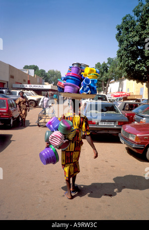 Donna venditore di strada equilibrando i suoi articoli di plastica della cucina sulla sua testa sulla strada per il mercato. Ouagadougou, Burkina Faso Foto Stock