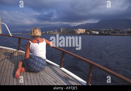 Cipro del Nord. Giovane donna una crociera su un caicco, con Kyrenia (Girne) città, porto e castello visibile in lontananza. Foto Stock