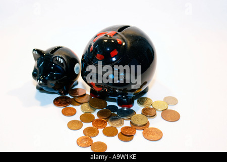 Due macchie nere salvadanaio suini circondato da monete Foto Stock