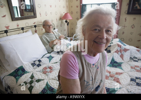 Senior sorridente donna seduta sul letto con degenti uomo senior Foto Stock