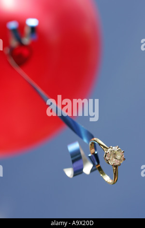 Solitaire anello di fidanzamento attaccato al nastro di un palloncino rosso a basso angolo di visione da vicino Foto Stock