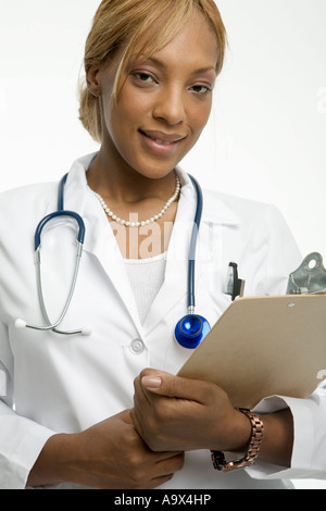 Giovane donna medico in camice bianco con un blocco appunti e uno stetoscopio sorrisi a fotocamera Foto Stock