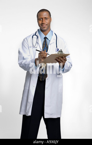 Giovane nero medico che indossa un mantello bianco e stetoscopio in scrittura su un blocco appunti Foto Stock