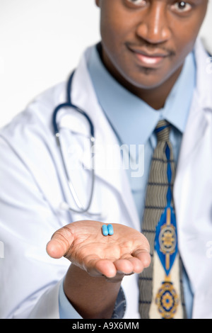 Dottore in camice bianco offre farmaci a un paziente. Il medico la mano e le capsule sono a fuoco ma il suo viso e corpo non è. Foto Stock