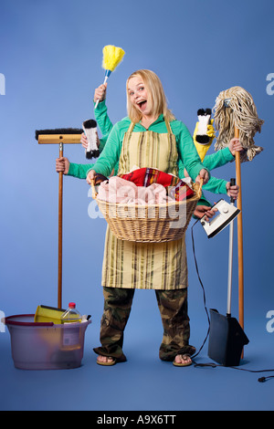 Donna con molti bracci impegnati in partite di casa tenere faccende tenendo spazzole e scope e un cesto della biancheria Foto Stock