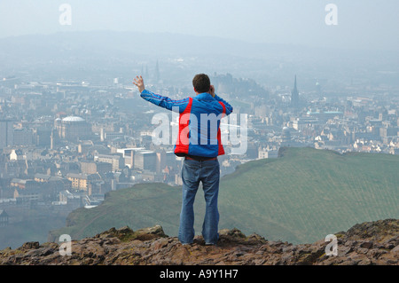 Un viandante colloqui su un telefono cellulare mentre guardando fuori alla vista di Edimburgo, Scozia, Regno Unito dalla sommità di Arthur Seat. Foto Stock