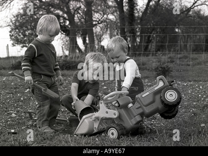 Immagine retrò di tre ragazzi che giocano insieme fuori in un giardino con un secchio di digrupo giocattolo e spade Inghilterra Regno Unito Gran Bretagna Foto Stock