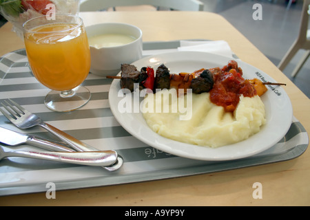 Vassoio ristorante IKEA con spiedini di carne alla griglia, purè di patate, salsa di pomodoro, succo d'arancia e piatto da dessert su un tavolo da pranzo. Foto Stock