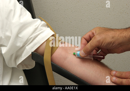 Un operatore sanitario preleva con attenzione il sangue dal braccio di un paziente utilizzando una siringa Foto Stock