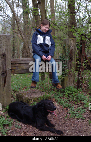 Ragazza seduta su un montante verticale in campagna con un labrador nero Foto Stock